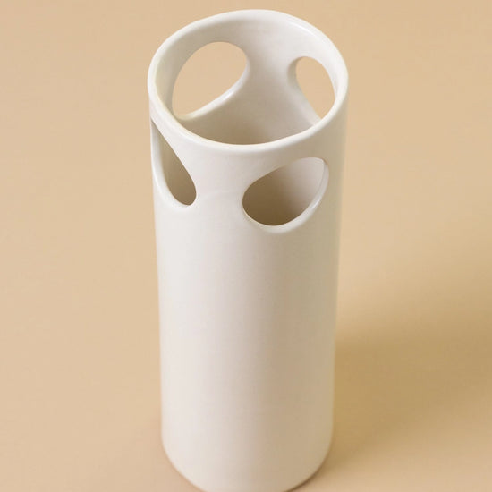 White ceramic vase with circular holes on a beige background