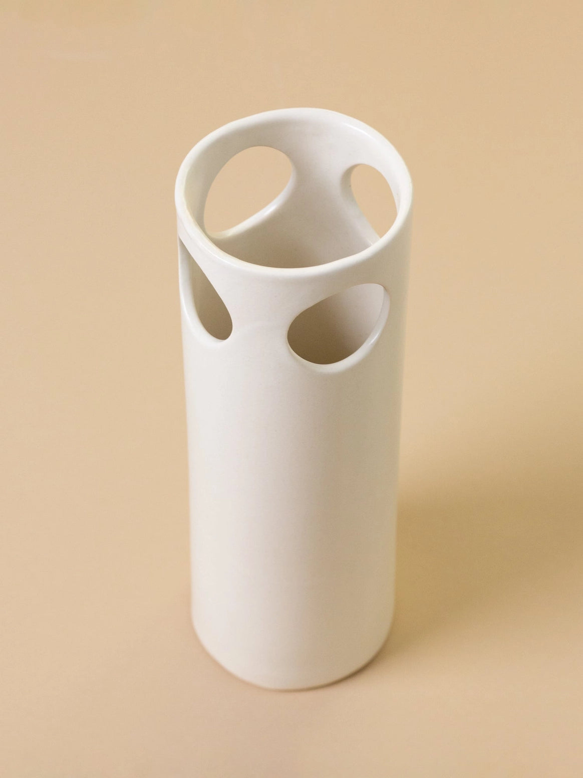 White ceramic vase with circular holes on a beige background