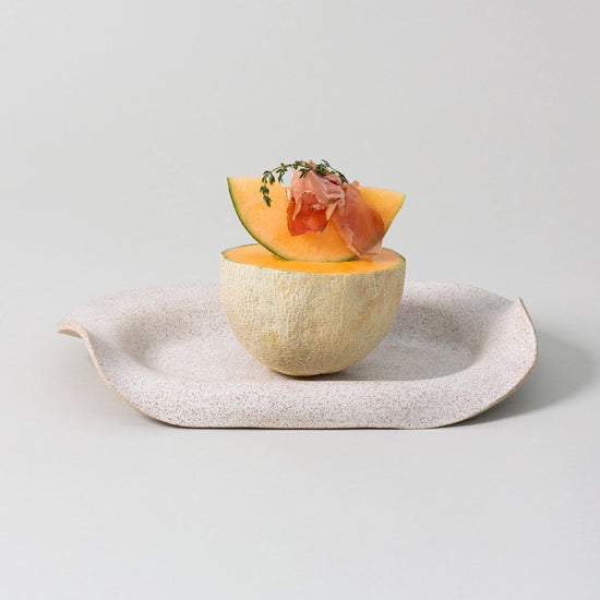 Melon half with a small dish inside on a light gray surface
