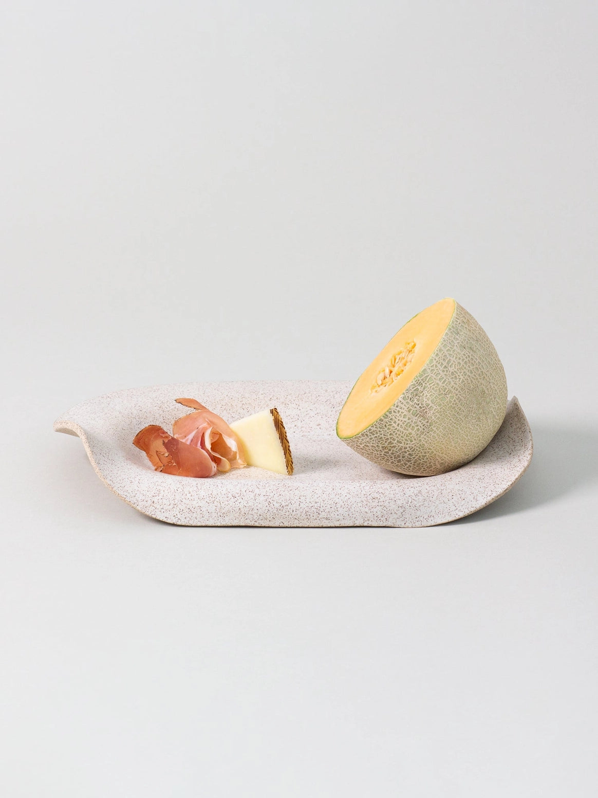 Melon half and prosciutto on a white plate with a light gray background