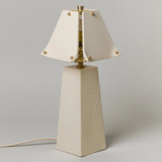 Table lamp with a beige base and white shade on a gray background