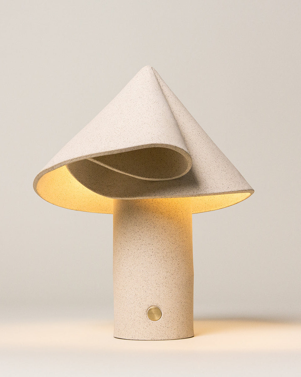 Sand-colored ceramic table lamp with a rounded base, photographed against a neutral background