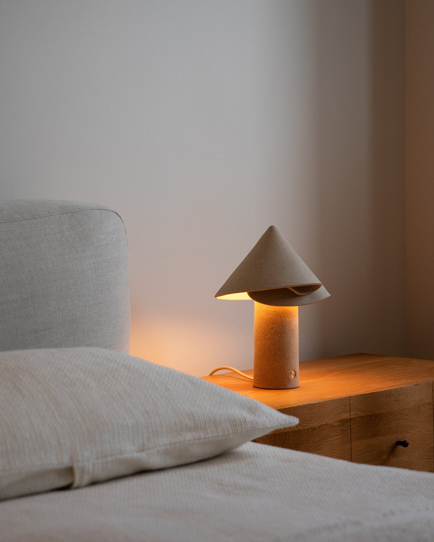 Bedroom scene with a bed and wooden nightstand featuring a lamp.