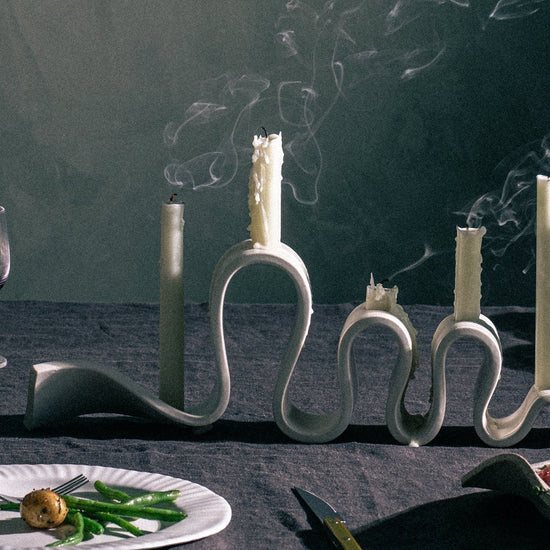 Decorative candle holders on a table with plates of food and cutlery, against a dark background.