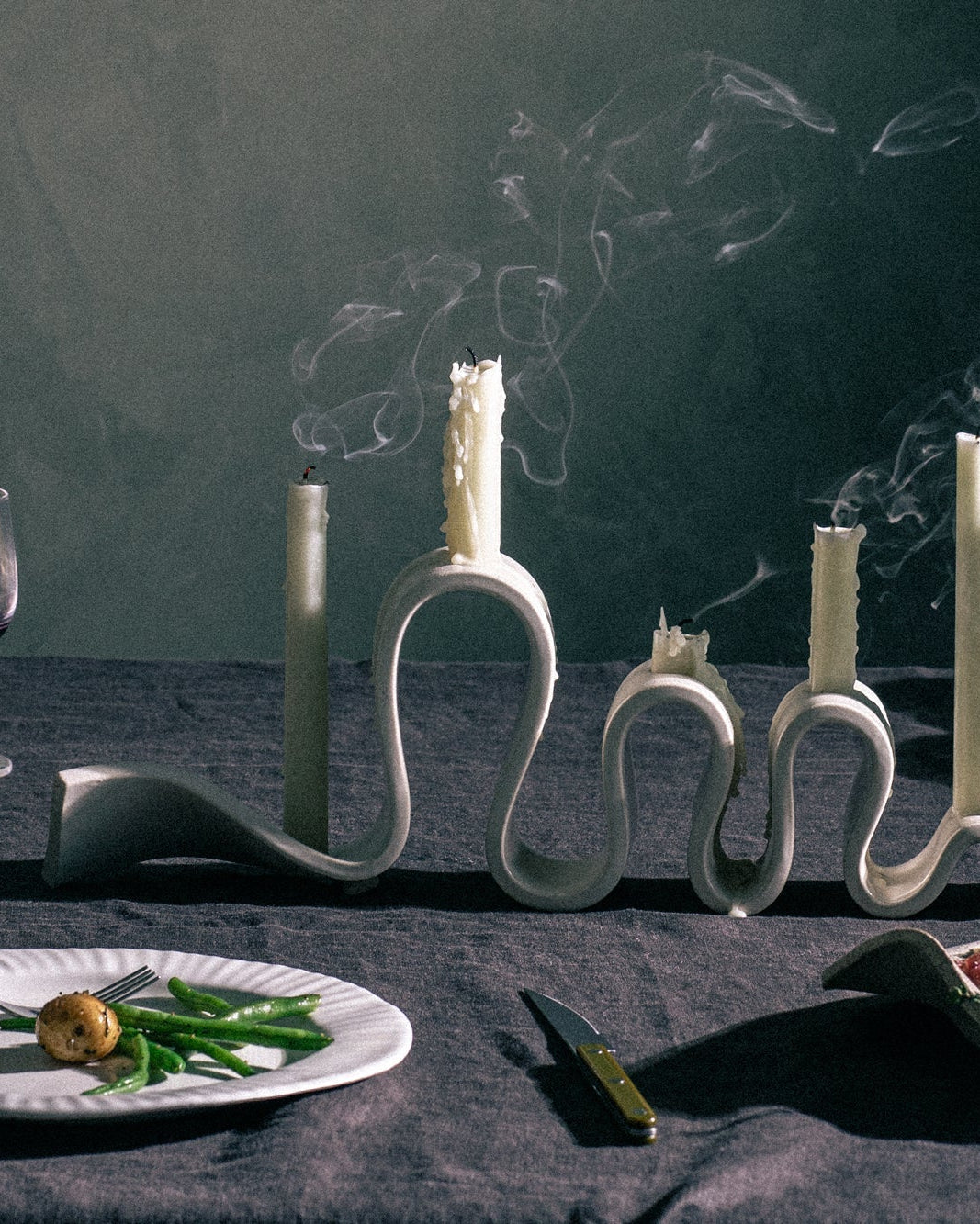 Decorative candle holders on a table with plates of food and cutlery, against a dark background.