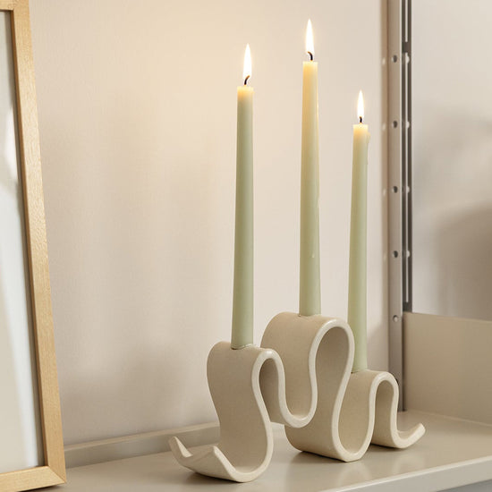 Decorative candle holder with three lit candles on a shelf next to a framed picture.