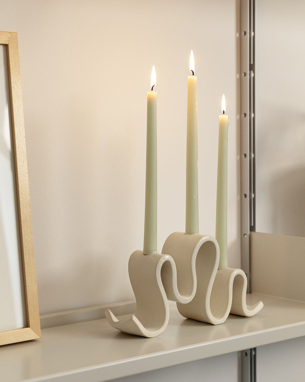 Decorative candle holder with three lit candles on a shelf next to a framed picture.