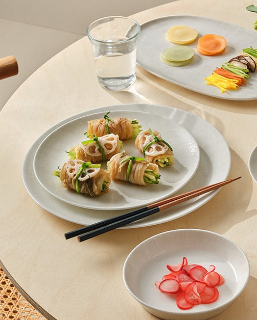 Round table set with various dishes of food and glasses on a neutral background