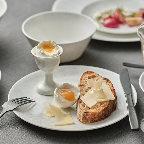 Breakfast setting with eggs, bread, and fruit on a gray tablecloth.