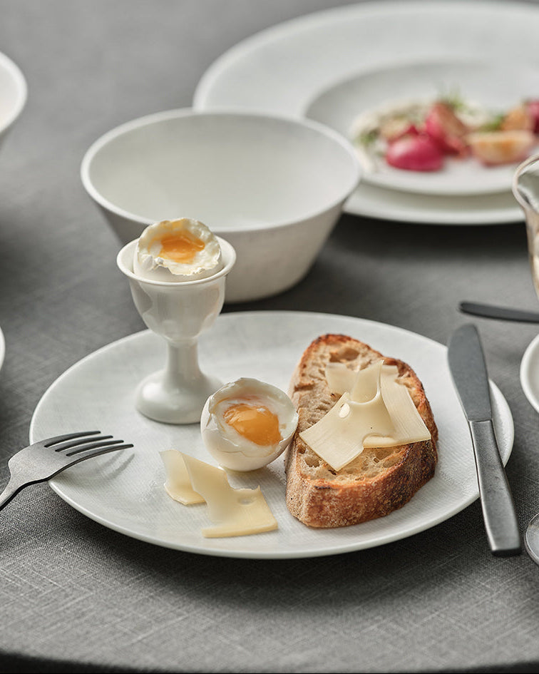 Breakfast setting with eggs, bread, and fruit on a gray tablecloth.