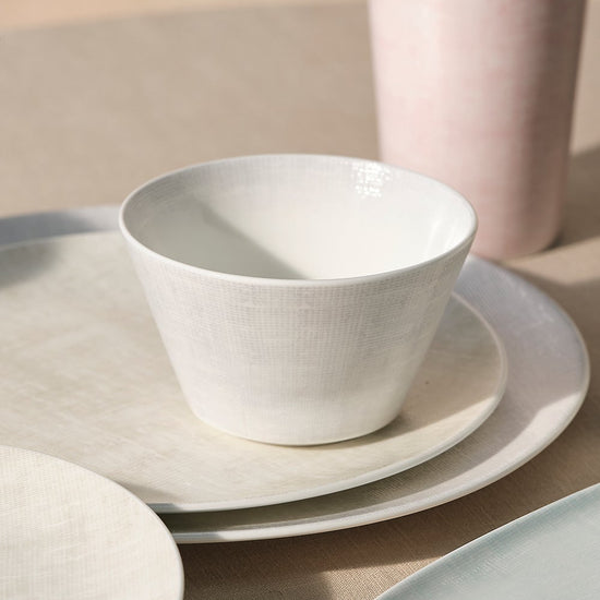 Set of ceramic dinnerware including bowls, plates, and cups on a neutral background.