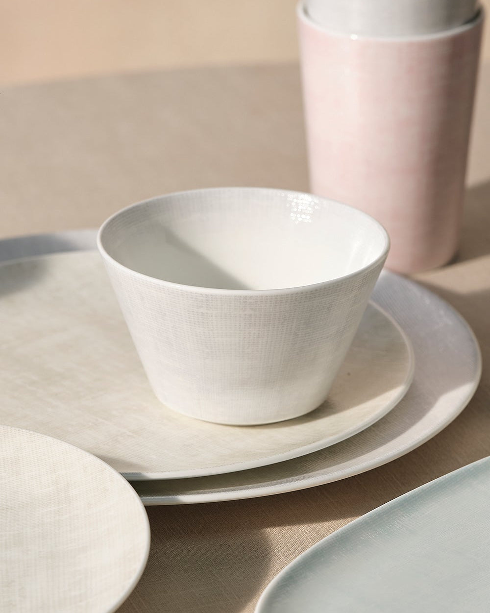 Set of ceramic dinnerware including bowls, plates, and cups on a neutral background.