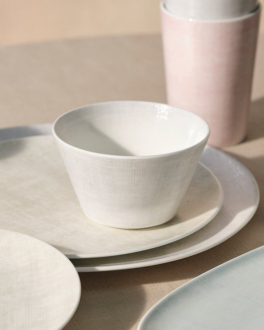 Set of ceramic dinnerware including bowls, plates, and cups on a neutral background.