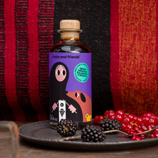 Bottle of 'Mates and Friends' product on a dark surface with red berries and blackberries, against a red and black striped background.