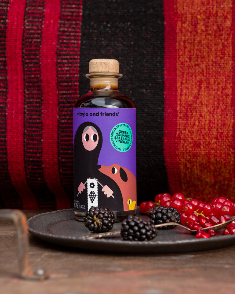 Bottle of 'Mates and Friends' product on a dark surface with red berries and blackberries, against a red and black striped background.