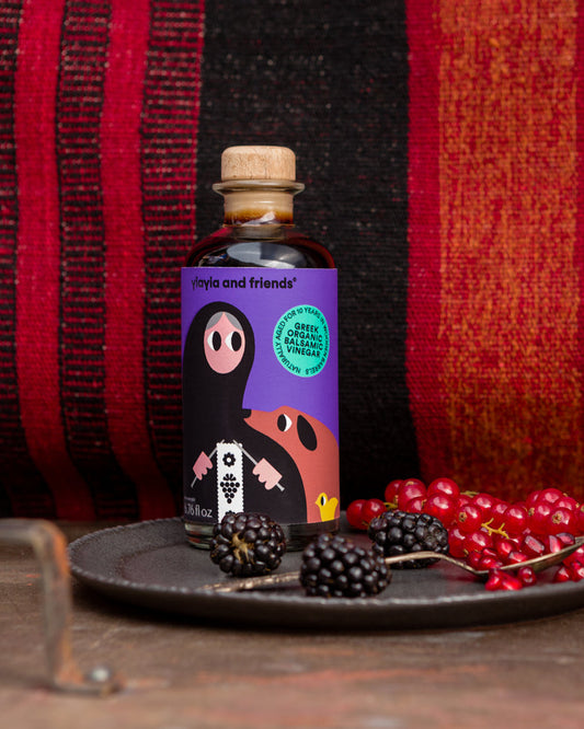 Bottle of 'Mates and Friends' product on a dark surface with red berries and blackberries, against a red and black striped background.
