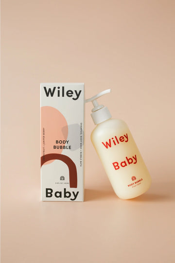 Wiley Baby Body Bubble cleanser bottle next to its packaging box, set against a solid peach-beige background.