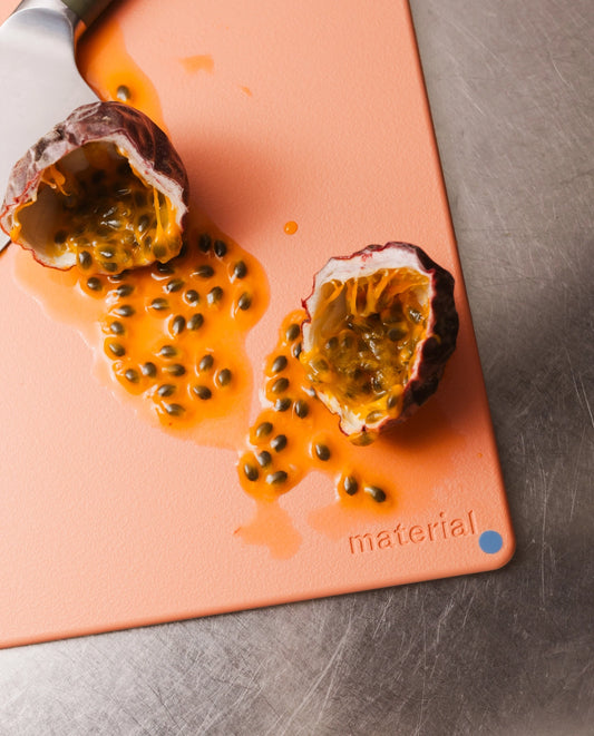 Halved passion fruit on a cutting board with visible brand 'material'.