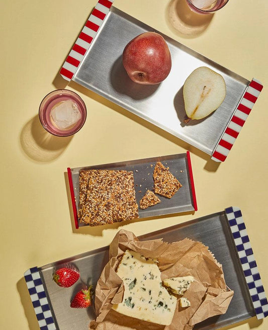 Trays with food items including crackers, cheese, fruit, and drinks on a yellow background