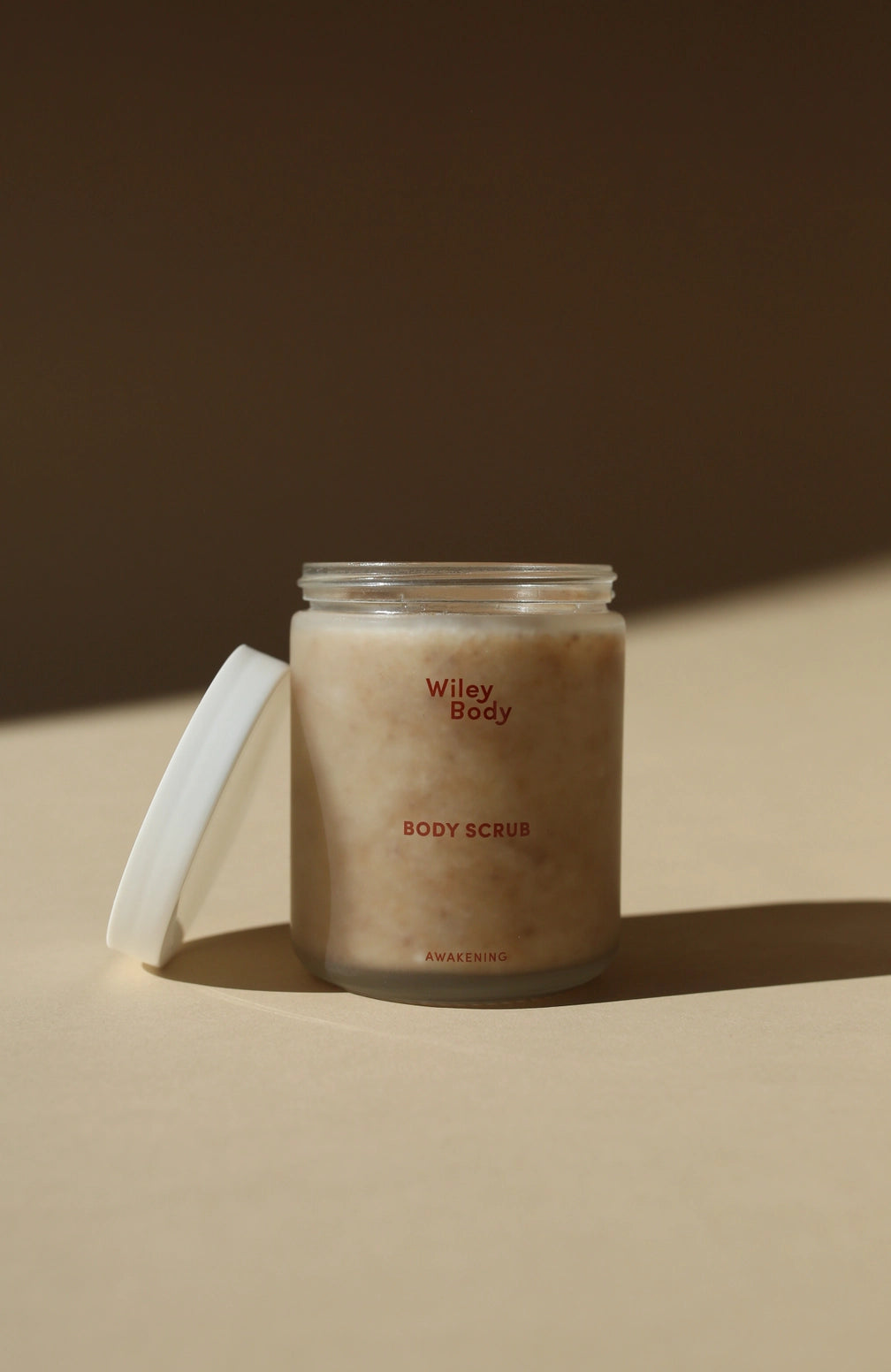 Jar of Wiley Body body scrub on a beige surface with a brown background