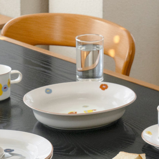 Dining table with ceramic dishes and a glass of water by a wooden chair.