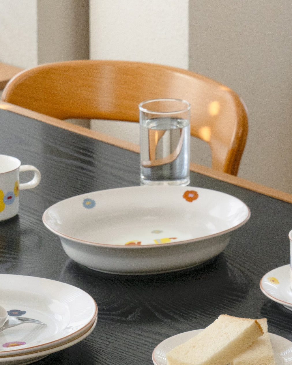 Dining table with ceramic dishes and a glass of water by a wooden chair.