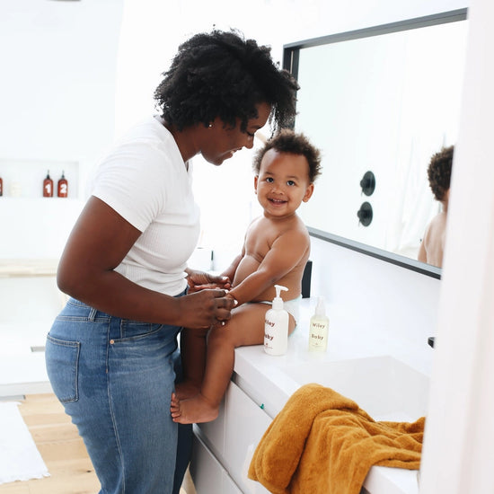 Woman and child in a bathroom with a yellow towel on a white surface.