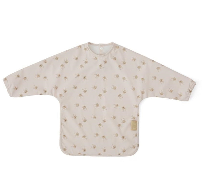Child’s polyester cape bib covered in an all-over pale pink rabbit print, with long sleeves and a snap-closure at the back neckline spread flat against a white background