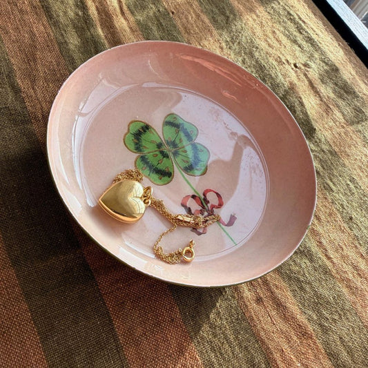 Pink ceramic dish with gold necklace and green clover leaf on a wooden surface
