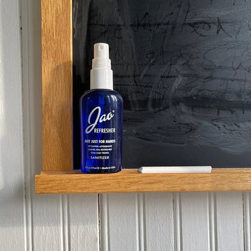 Blue bottle of Jao Refresher sanitizer on a wooden shelf with a chalkboard background